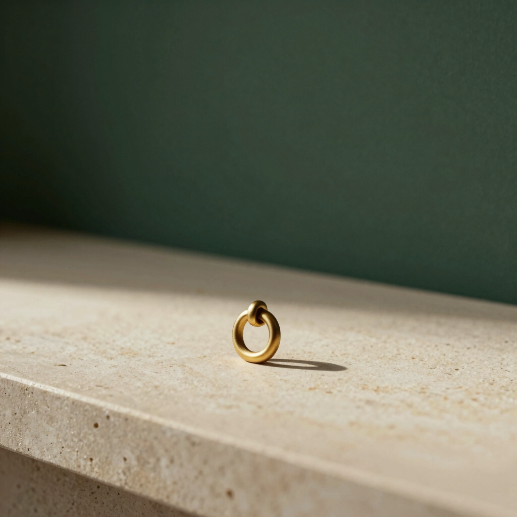 Side-lit minimalist interior with a single matte gold metal D-ring resting on a warm ivory stone surface, soft architectural shadows, serene and quiet luxury aesthetic.